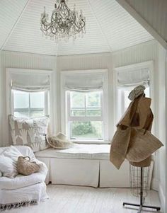 a room with white furniture and chandelier hanging from it's ceiling in front of two windows