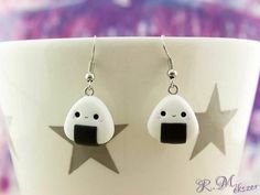 a pair of earrings with black and white designs on them sitting in front of a cup