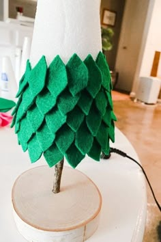 a small christmas tree made out of felt sitting on top of a white table next to a lamp