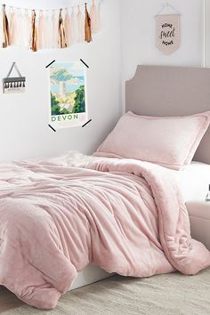 a bed with pink comforter and pillows in a white room next to a window