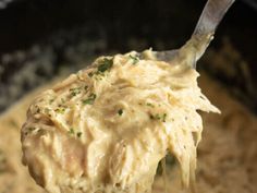 a spoon full of mashed potatoes being lifted from a pot with gravy