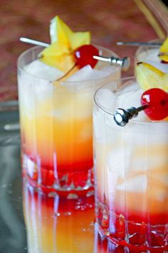 two glasses filled with drinks and garnished with pineapples, cherries, and watermelon