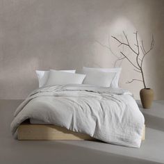 the bed is made up with white linens and pillows, along with two vases