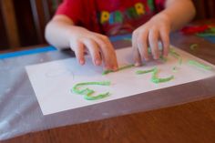 a young boy is making letters with green crayons on a sheet of paper