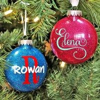 two ornaments hanging from a christmas tree with name written on one ornament and the other