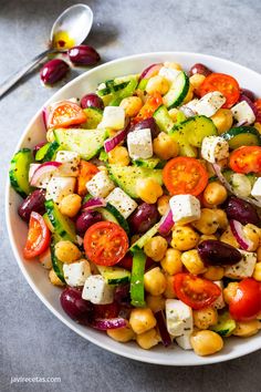 a white bowl filled with chickpeas, cucumber, tomatoes and olives