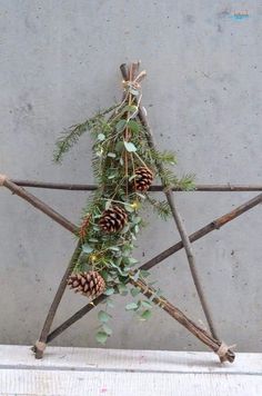 a star made out of sticks with pine cones and greenery hanging from it's sides