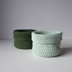 two crocheted baskets sitting next to each other on a white counter top, one is green and the other is light blue