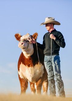 a man standing next to a brown and white cow on top of a dry grass field