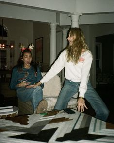 two women are sitting on a couch and one is holding her hand out to the other