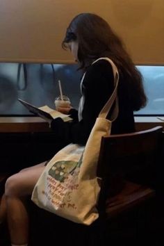 a woman sitting in a chair with a book and bag on her lap while reading