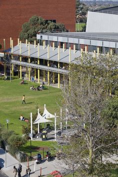 people are sitting on the grass in front of a building with yellow poles and white tents