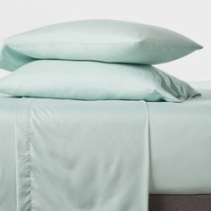 two pillows are stacked on top of each other in front of a bed with light green sheets