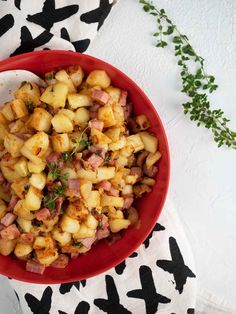 a red bowl filled with potatoes on top of a black and white table cloth next to a plant