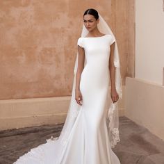 a woman in a white wedding dress with a veil on her head standing next to a wall