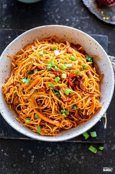 someone is holding a spoon over a bowl of noodles with carrots and green onions