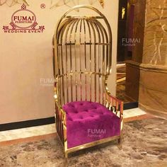 a gold birdcage sitting on top of a marble floor next to a purple chair