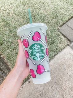 a hand holding a starbucks cup with pink hearts and candy on the outside, in front of some grass