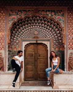 a man and woman sitting on steps in front of an ornate building with wooden doors