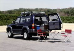 an suv parked in a parking lot next to a table with chairs and luggage on it