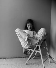 a woman sitting in a chair with her legs crossed on the floor and reading a book