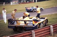 some men are standing around a race car on the track with other people looking at it