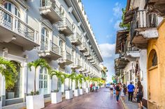 people are walking down the street in front of some white and yellow buildings with balconies