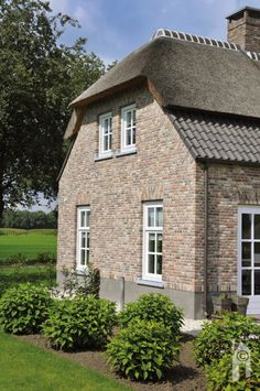 a brick house with white windows and a thatched roof