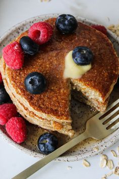 a pancake with berries and blueberries is on a plate next to a fork