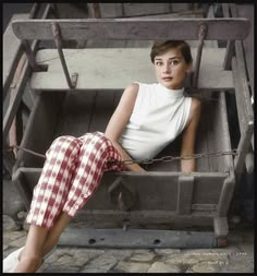 a woman sitting on top of an old wooden crate with her legs crossed and wearing red checkered pants