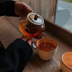 a person pouring tea into a cup on a wooden table