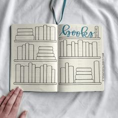 a hand holding an open book on top of a white sheet with bookshelves