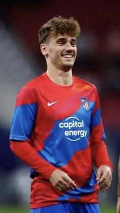 a young man standing on top of a soccer field wearing a red and blue uniform