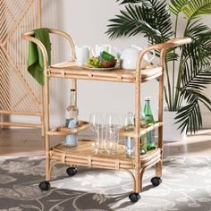 a bamboo serving cart with drinks and glasses on it next to a potted plant