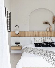 a bed with white sheets and pillows in a room next to a wall mounted clock