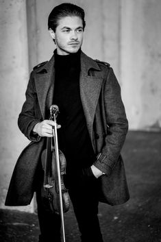 a man is holding a violin and posing for a black and white photo with his hands in his pockets