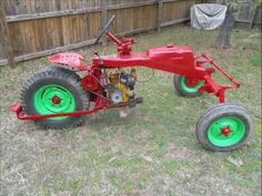 a red tractor with green wheels parked in the grass next to a fence and tree