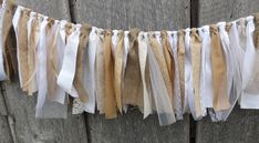 some ribbons are hanging on the side of a wooden fence with white and beige ribbon