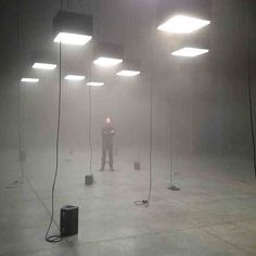 a man standing in the middle of an empty room with lights on either side of him