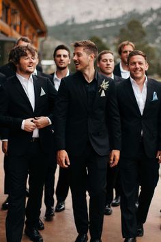 a group of men standing next to each other wearing black suits and white shirts with blue lapels