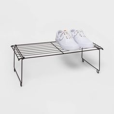 a pair of white tennis shoes sitting on top of a black metal shoe rack,