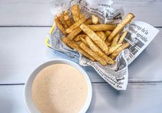 french fries and dipping sauce in a bowl on a white wooden table with newspaper wrappers