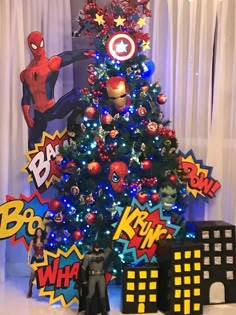 a christmas tree decorated with superheros and other holiday decorations is displayed in front of a curtained window