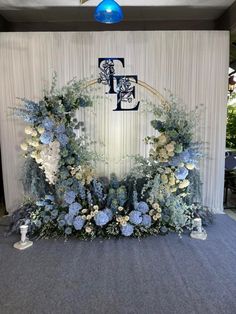 an arrangement of blue flowers and greenery is displayed on the floor in front of a wall