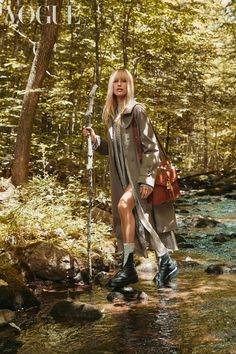 a woman is standing in the water holding a stick and wearing raincoat with boots