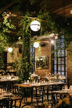 an indoor dining area with tables and chairs covered in greenery, surrounded by hanging lights