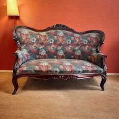 a couch sitting in front of a lamp on top of a carpeted floor next to a red wall