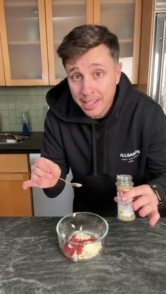 a man in a black hoodie is eating food from a glass bowl with a spoon