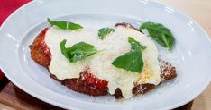 a white plate topped with meat covered in sauce and cheese next to green leaves on top of it