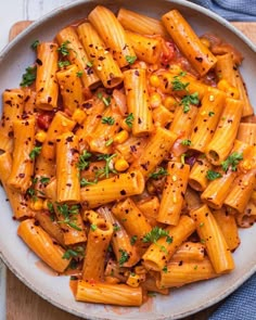 pasta with corn and parsley in a white bowl on a wooden table next to a blue napkin